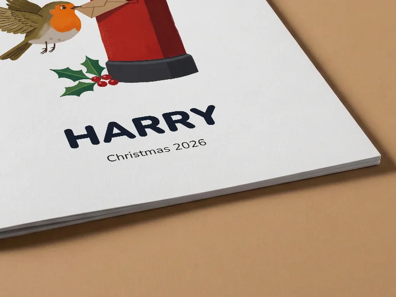 Close-up of a Christmas colouring book cover with a robin, a post box and the name Harry, on tan card, showing the cover card and its thin page edge.