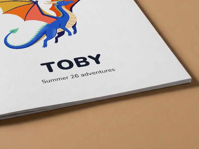 Close-up of a colouring book cover with a dragon and the name Toby, on tan card, showing the cover card and its thin page edge.