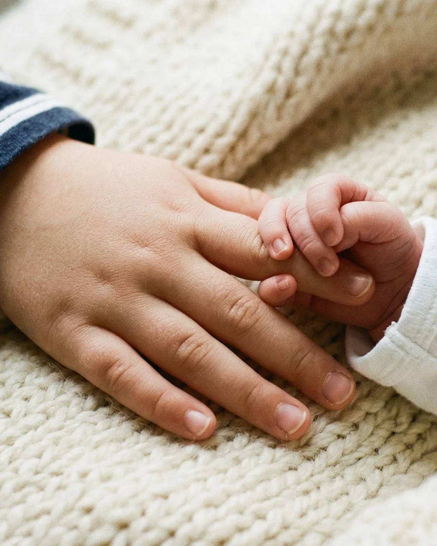 A newborn's hand gripping an older child's finger